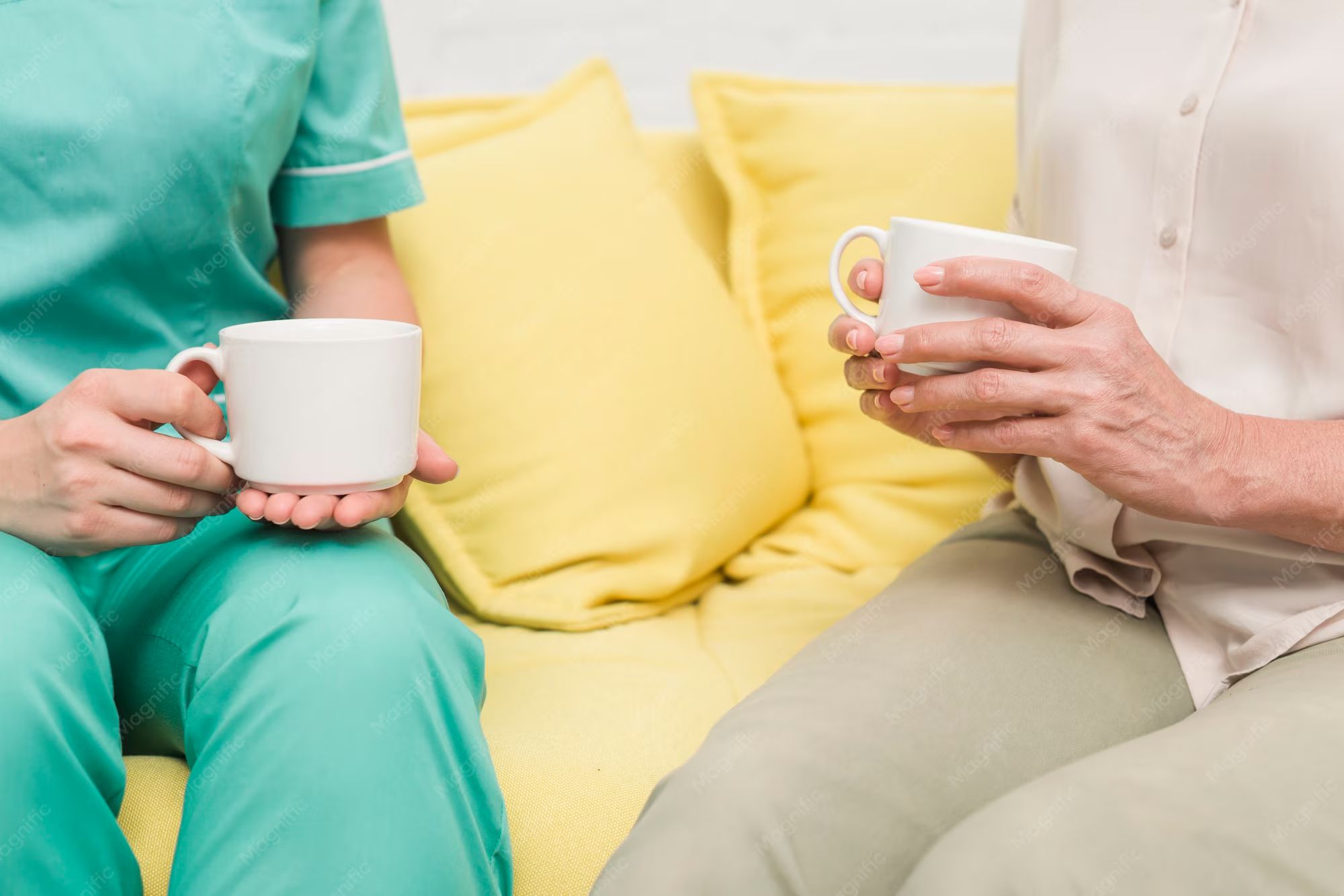 A nurse and an older resident sharing a cup of tea on a sofa